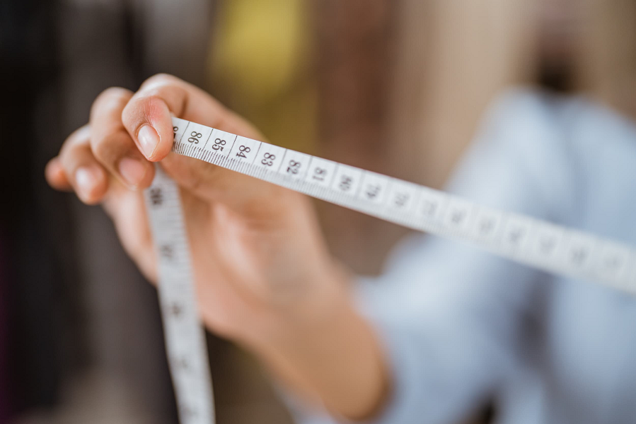 A woman holds a flexible fabric measuring tape.